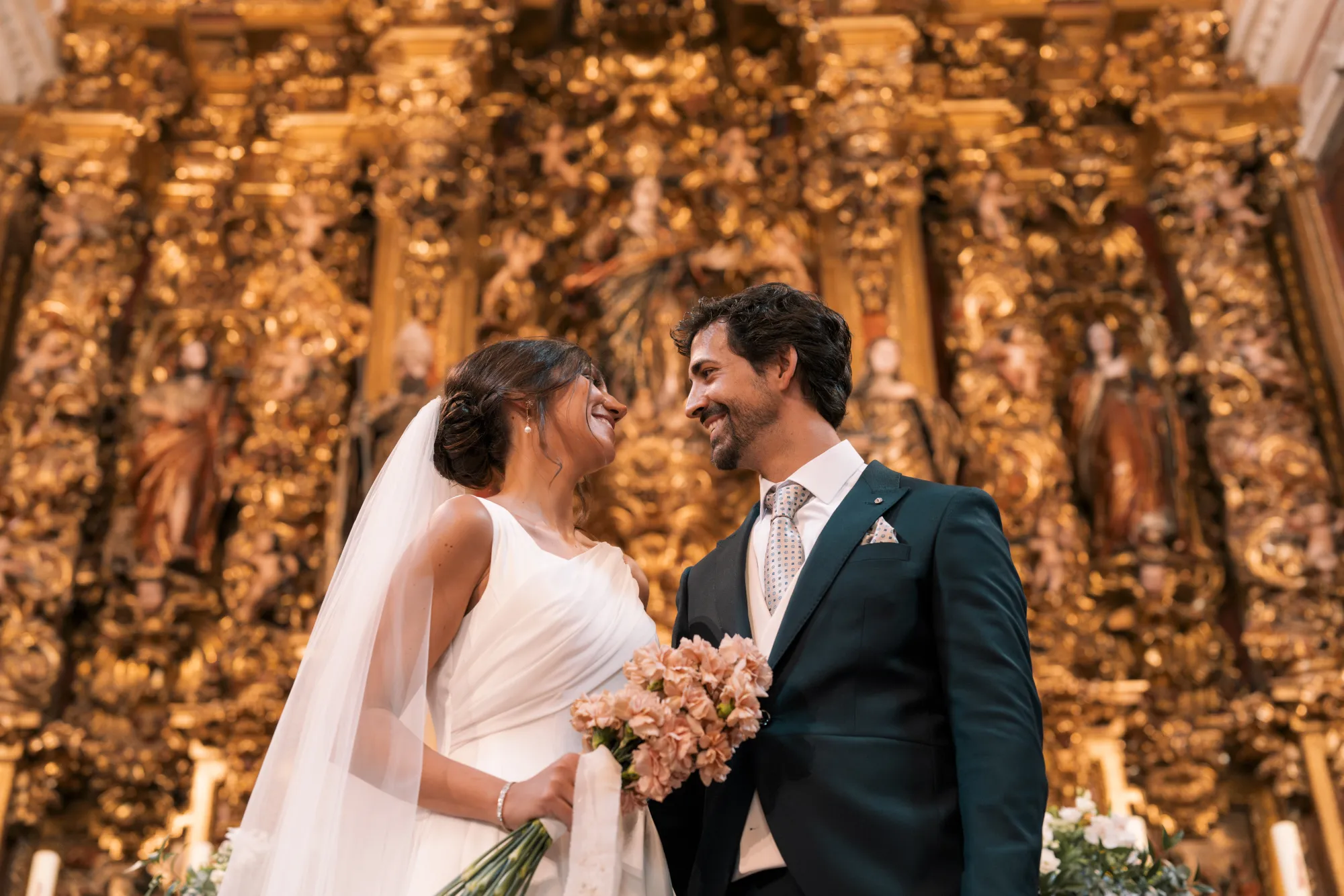 Los novios ríen frente al retablo dorado de la iglesia