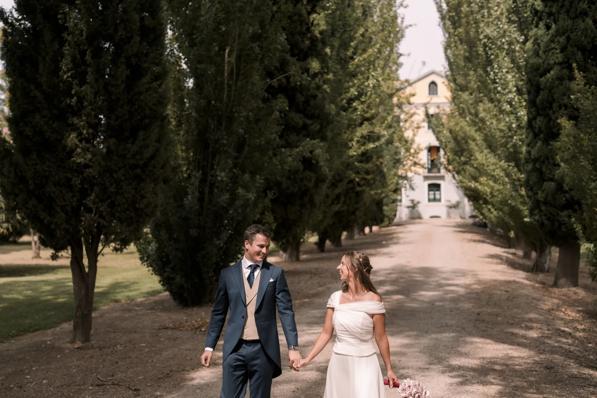 Fotografía de boda de DOME: los novios caminan por un paseo arbolado