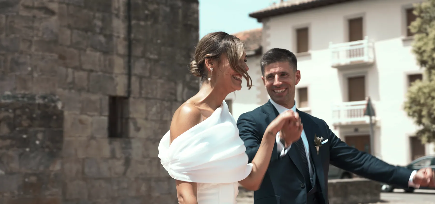 Fotograma de un vídeo de boda de DOME: los novios ríen frente a un edificio blanco